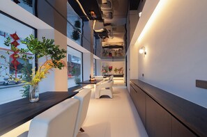 Ein modernes Interieur mit einem langen Esstisch, weiß gepolsterten Sitzgelegenheiten und Blick durch große Fenster.