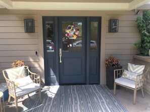 A front door with a 'No Soliciting' sign, two wicker chairs with cushions, a doormat, and a potted plant on the porch. - Spacious 4-bedroom house on a quiet wooded cul de sac (Boulder)