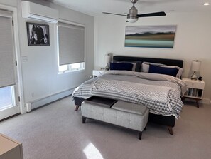 Ein Schlafzimmer mit Bett, Nachttischen, einer Lampe, einem Bilderrahmen, einem Deckenventilator und einem Fenster mit Jalousien.