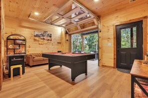 A cozy room with a pool table, a sofa, and a door leading to an outdoor area. - Modern Rustic Cabin - Hot tub, Shuffleboard, Pool Table Nestled in Trees (Logan)