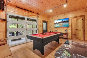 Ein Holzinnenraum mit Billardtisch, Fernseher und einer Tür, die auf einen Balkon führt.