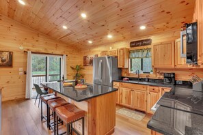 Eine Holzhütte mit einer Küche, einer zentralen Kochinsel, Barhocker, einem Kühlschrank und einer Kaffeestation.