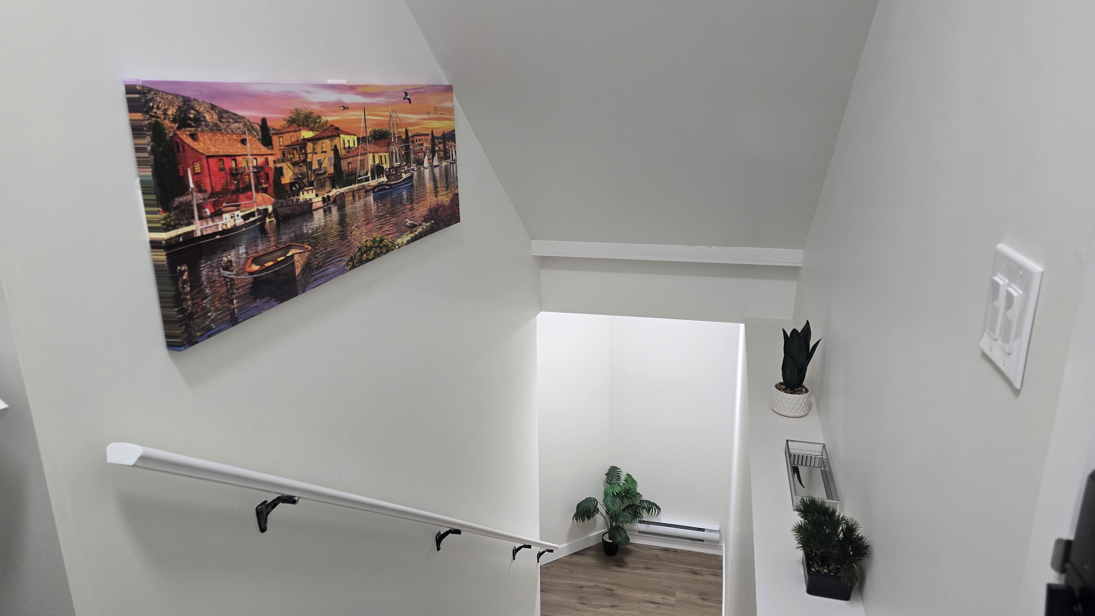 En trappe med et maleri af en havneudsigt, en potteplante og en lyskontakt på væggen.