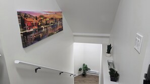 Eine Treppe mit einem Gemälde einer Haflandschaft, einer Zimmerpflanze und einem Lichtschalter an der Wand.