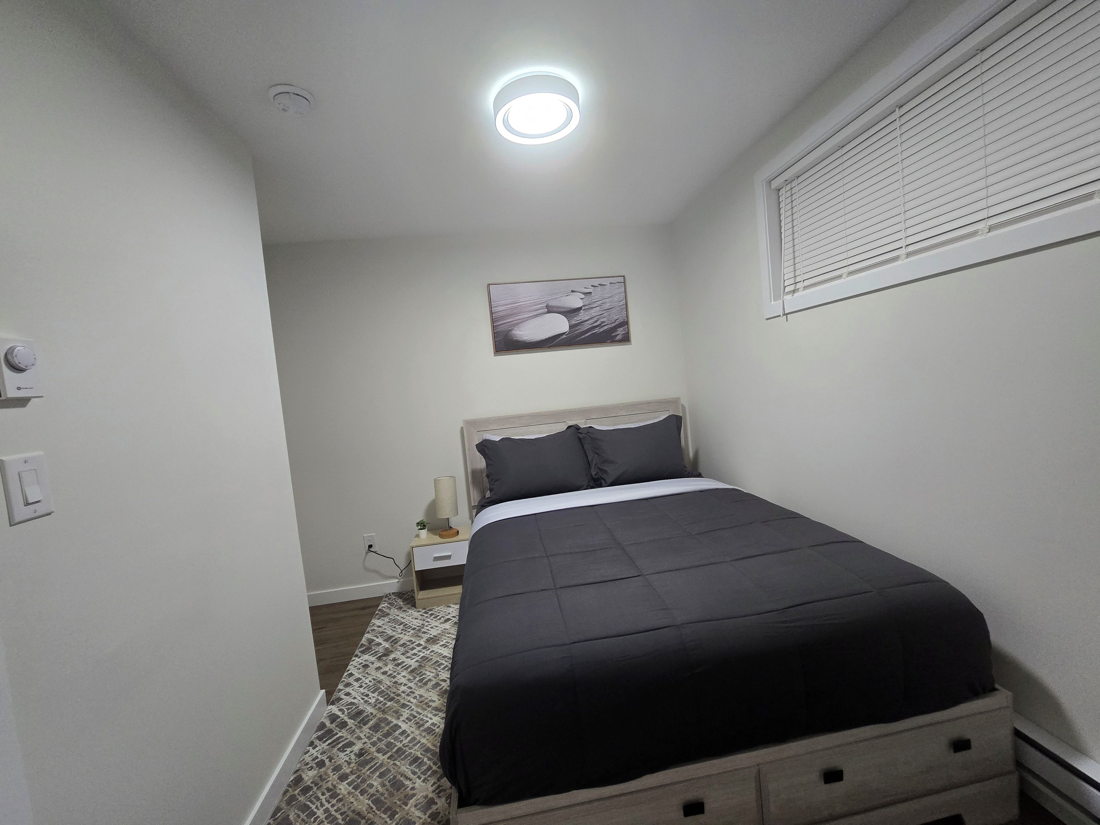 A bedroom with a bed, bedside table, lamp, and a painting on the wall.