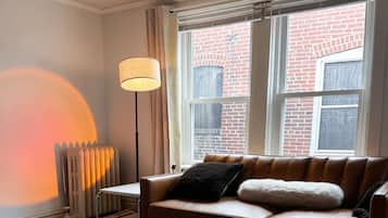 En hyggelig stue med en brun lædersofa, et glasbord, en gulvlampe og en radiator.
