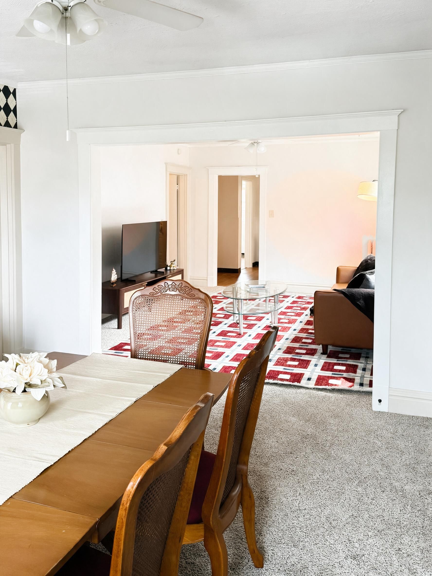 Un coin repas avec une table et des chaises en bois, un téléviseur et un tapis à motifs.