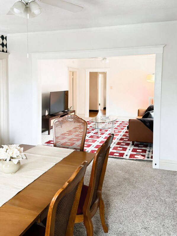 A dining area with a wooden table and chairs, a television, and a patterned rug.