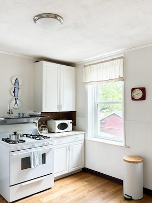 A kitchen with white cabinets, a stove, a microwave, and a window with a view of greenery outside. - Retro 3BR in Historic Shaw · Near Tower Grove Park (St. Louis)