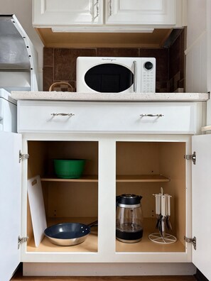 Una cocina con microondas en la encimera, un colador verde, una sartén negra y una cafetera.