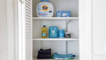 A white closet with shelves containing Tide laundry detergent, a bottle of dish soap, and folded clothes.