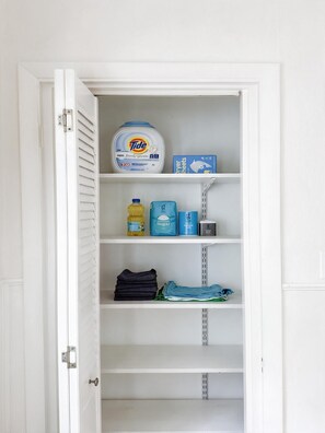 A white closet with shelves containing Tide laundry detergent, a bottle of dish soap, and folded clothes. - Retro 3BR in Historic Shaw · Near Tower Grove Park (St. Louis)