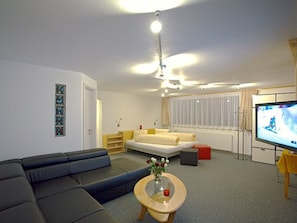 A modern living room with a sofa, a coffee table with a vase, a television, and a bed with a window. - Eden 4 OG Brunegghorn, (Grächen), by Interhome (Grächen)