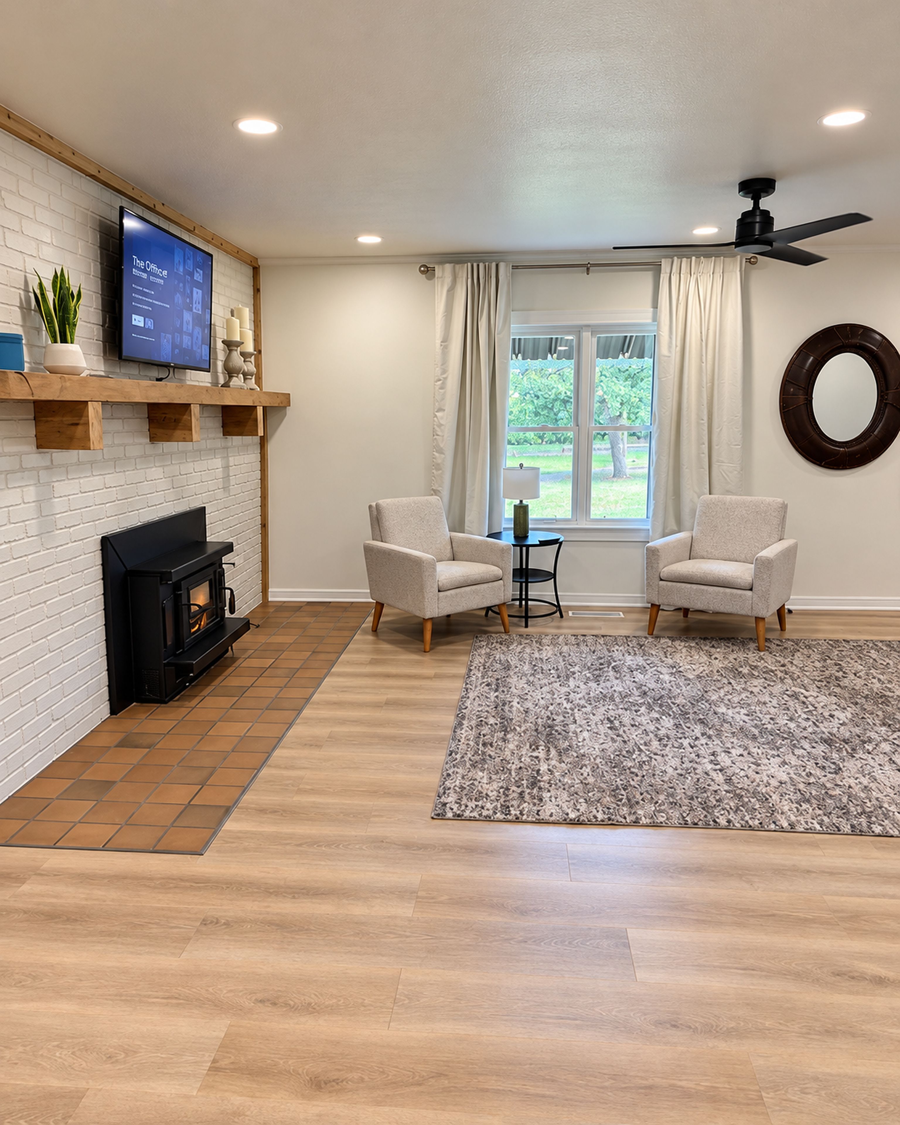 A living room with a fireplace, two armchairs, a television, and a ceiling fan.