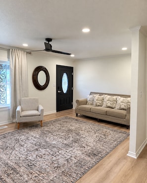 A spacious living room with a large rug, a sofa, a chair, a ceiling fan, and a door with a decorative glass panel. - Lovely 3-bedroom house just minutes from Downtown Graham (Graham)