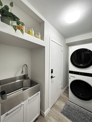 A compact kitchen with a sink, cabinets, a door, and a washing machine. - Westmount Retreat | 5 Bedrooms, 2 Baths & Free Parking (Hamilton)