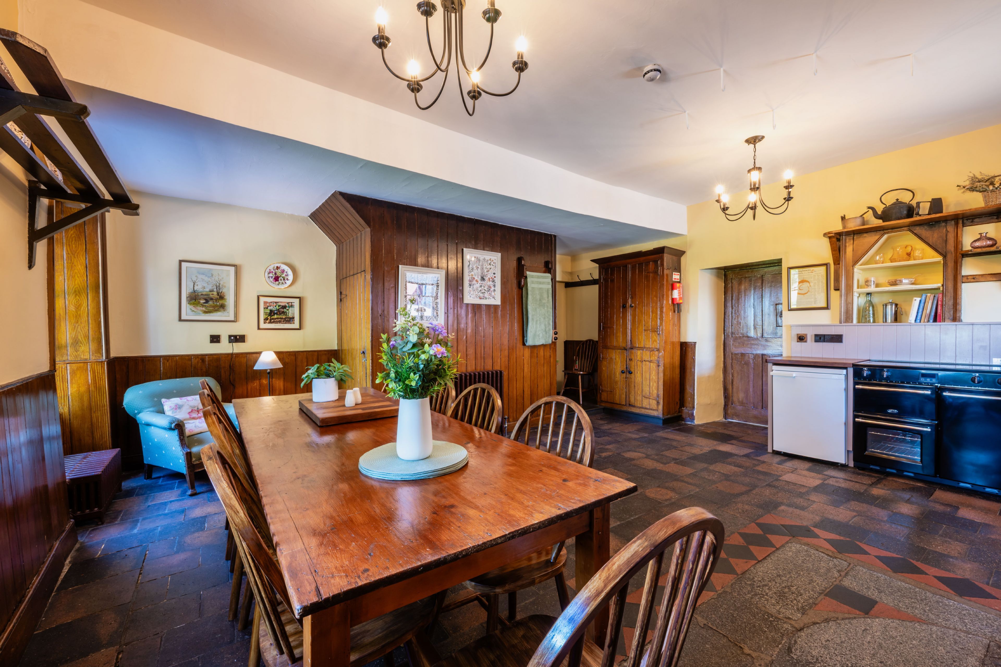 A dining area with a wooden table and chairs, a vase with flowers, and a kitchen with modern appliances.