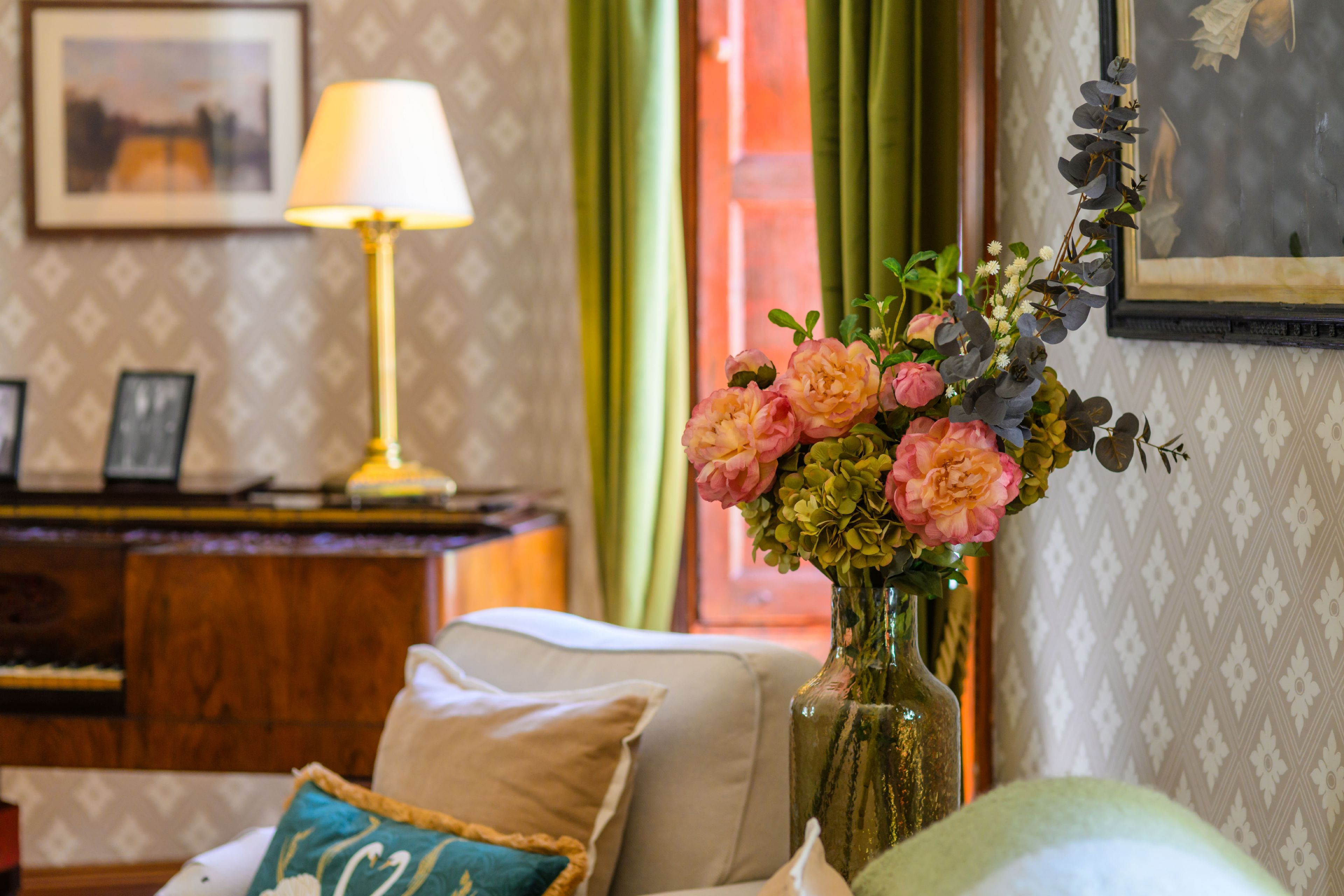 A room with a sofa, a vase with flowers, a lamp, and a framed picture on the wall.