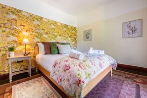 A neatly made bed with floral bedding, a bedside table with a lamp, and a floral-patterned wall. - Tullymurry House - Fabulous 5-bedroom Country House and Spa - 4 Star (Newry)
