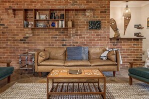 A cozy living room with a brick wall, a leather sofa, a coffee table, and a bookshelf. - Le Souef Authentic MR Retreat With Cosy Fire (Margaret River)