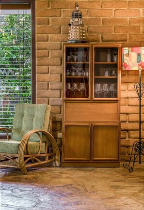 A room with a brick wall, a wicker chair, a wooden cabinet with glassware, and a metal stand. - Le Souef Authentic MR Retreat With Cosy Fire (Margaret River)