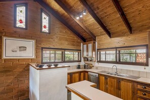 A kitchen with wooden beams, a brick wall, and a window with blinds. - Le Souef Authentic MR Retreat With Cosy Fire (Margaret River)