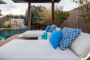 Een terras bij het zwembad met een houten dek, een stenen muur en een houten omheining.