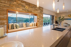 A kitchen with a stone backsplash, a built-in bench with cushions, a large window, and a sink. - Fragrant Harbour with stunning ocean views (Gnarabup)