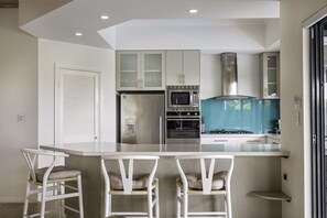 A modern kitchen with a central island, white cabinetry, and a stainless steel range hood. - Baudin House By The Beach With Views (Gnarabup)
