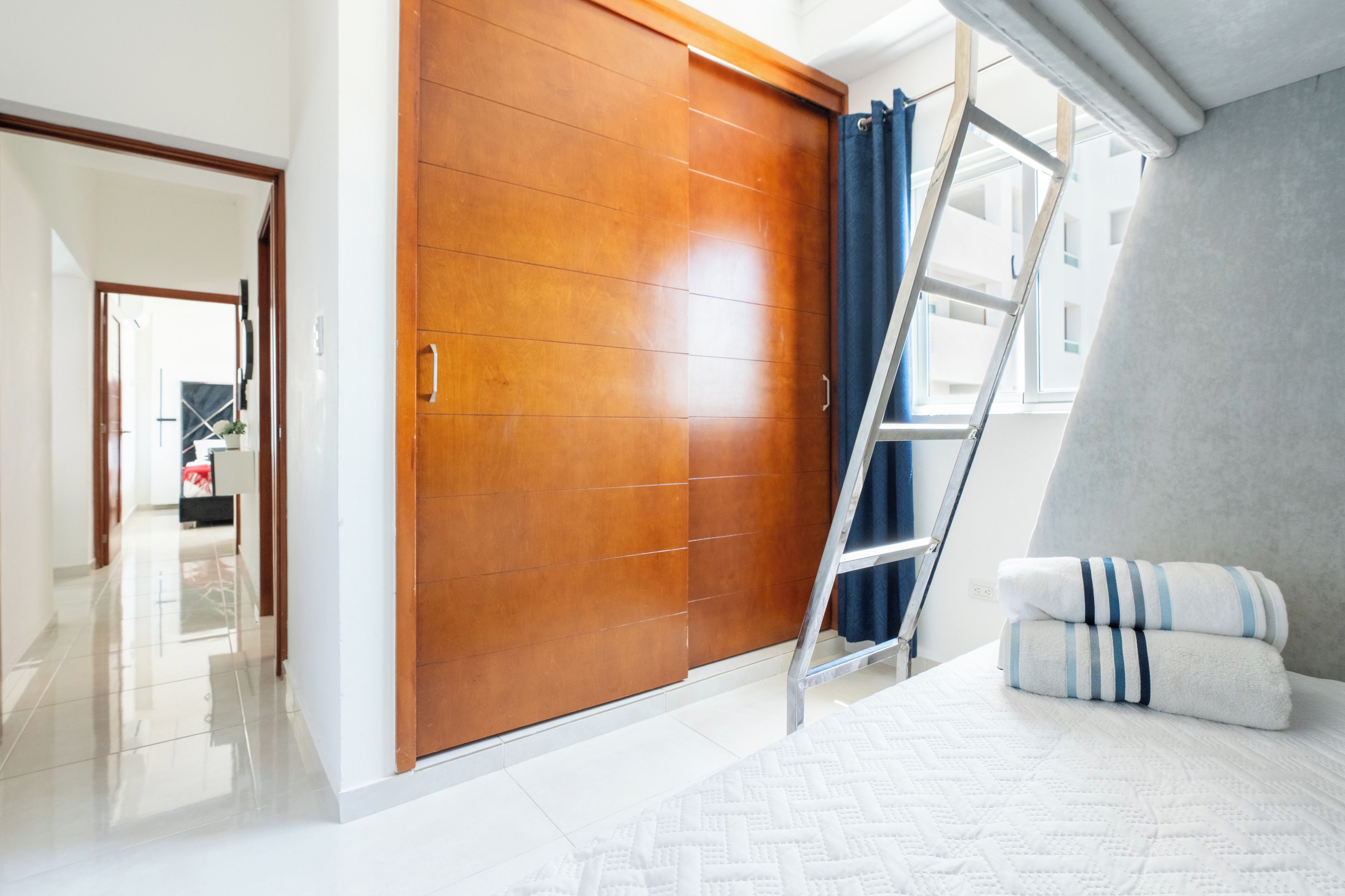 Une chambre avec une armoire en bois, une échelle et un lit avec des oreillers.