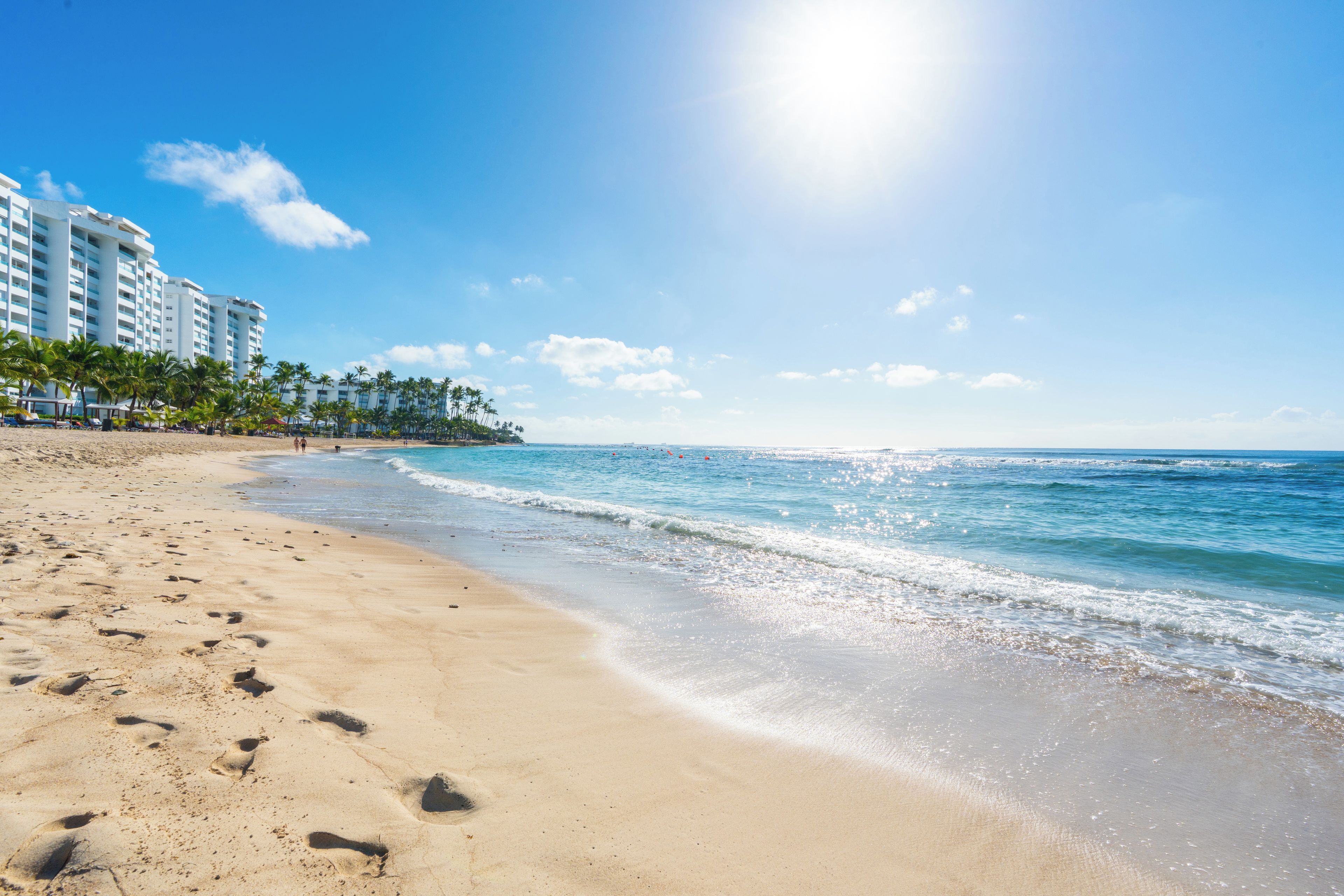 A beach with footprints, a clear sky, and a building in the background.