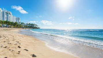 A beach with footprints, a clear sky, and a building in the background.