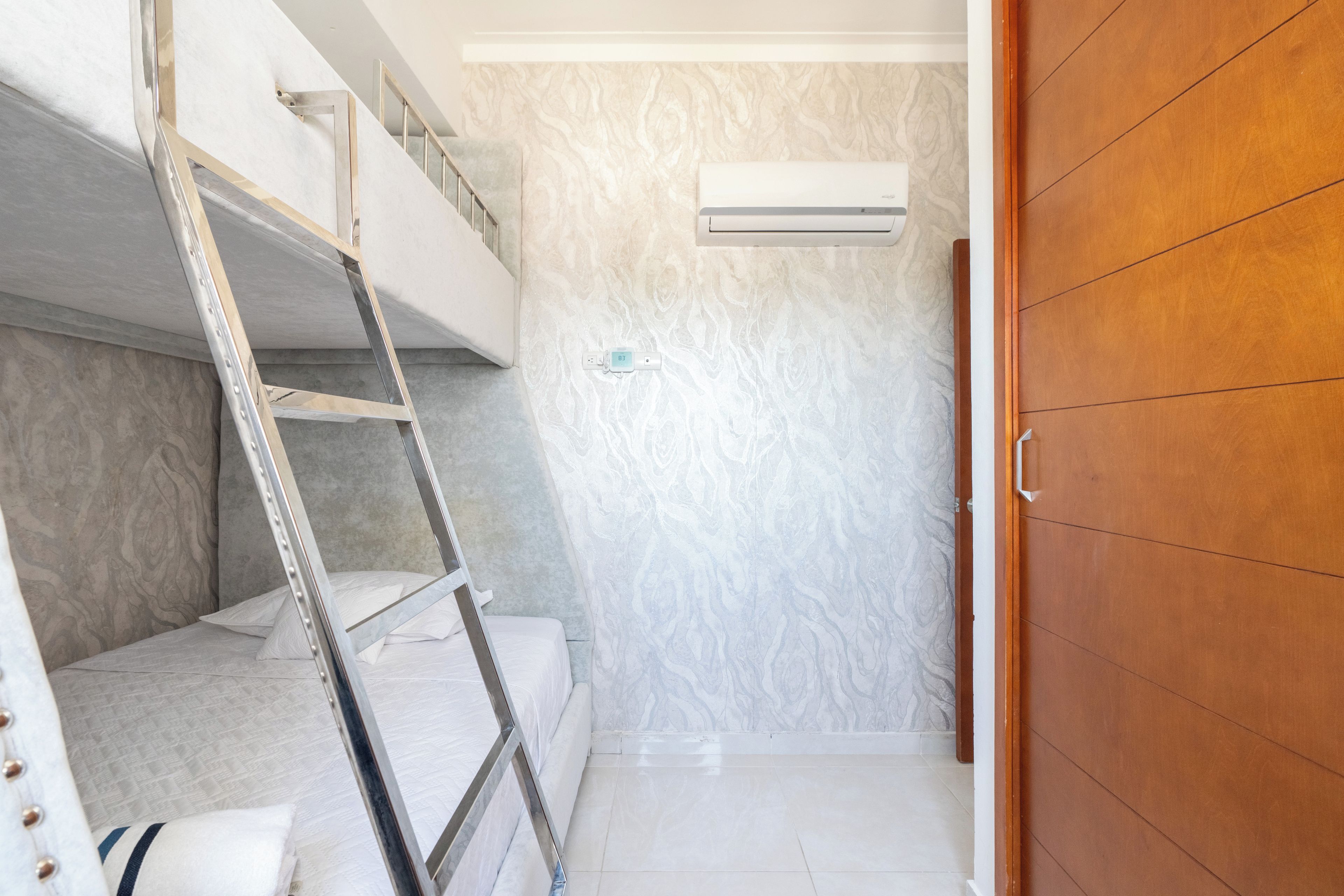 A room with a bunk bed, a ladder, an air conditioning unit, and a wooden wardrobe.