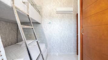 A room with a bunk bed, a ladder, an air conditioning unit, and a wooden wardrobe.