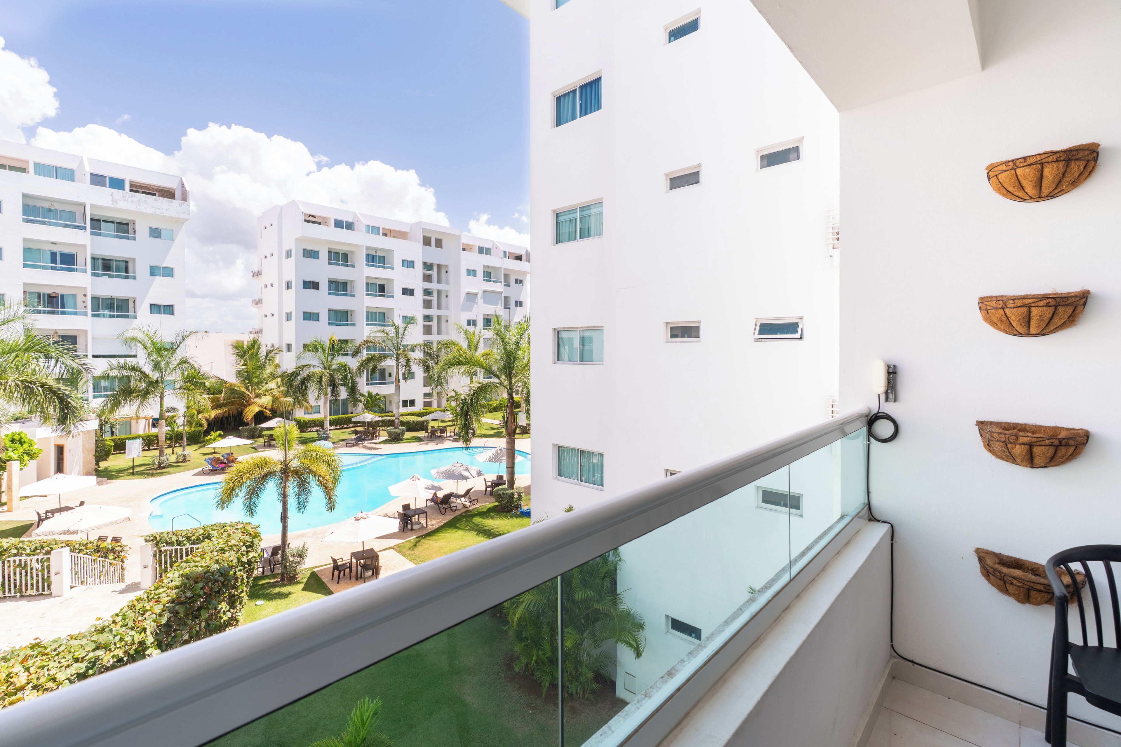 A balcony with a view of a swimming pool, palm trees, and a white building with multiple windows.
