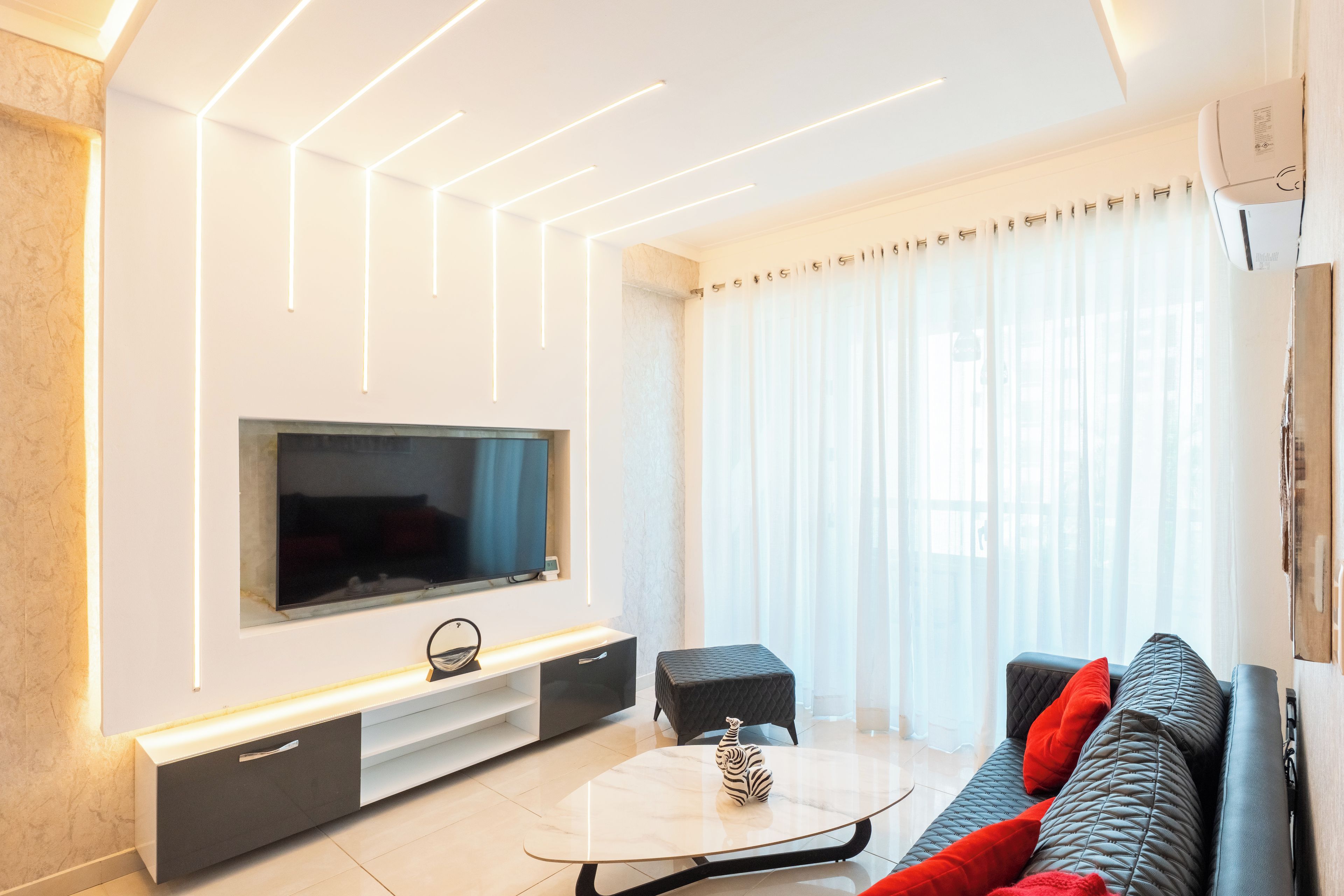 A modern living room with a flat-screen TV, a coffee table, and a sofa with red cushions.