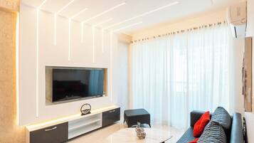 A modern living room with a flat-screen TV, a coffee table, and a sofa with red cushions.