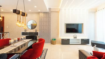 A modern living room with a dining area, a flat-screen TV mounted on the wall, and a chandelier.
