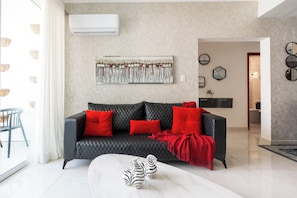 Un salon moderne avec un canapé en cuir noir, des coussins rouges, un vase à motifs zébrés et un grand tableau abstrait accroché au mur.