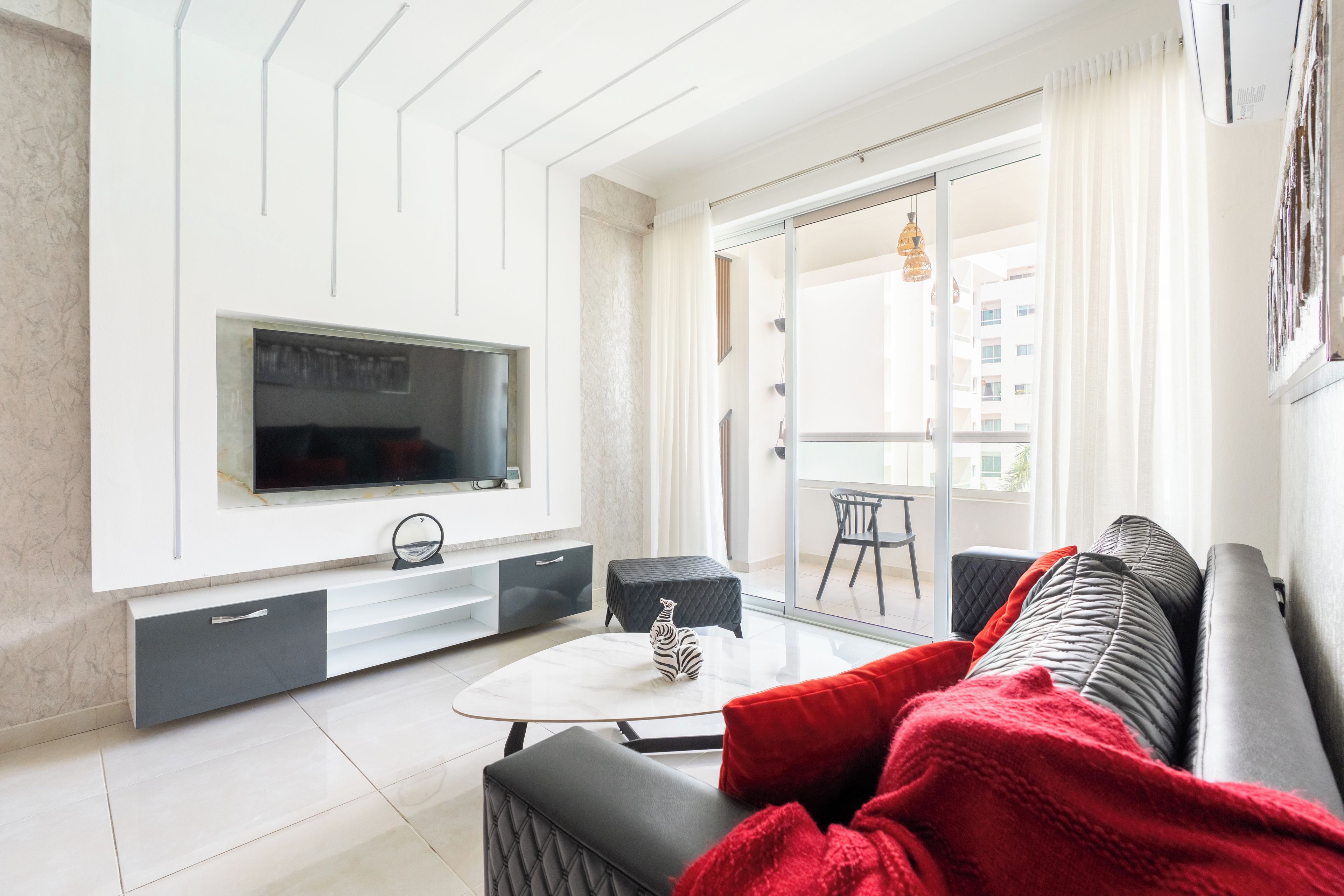 Una sala de estar moderna con un televisor de pantalla plana, un sofá, una mesa de centro y un balcón con vistas a edificios.