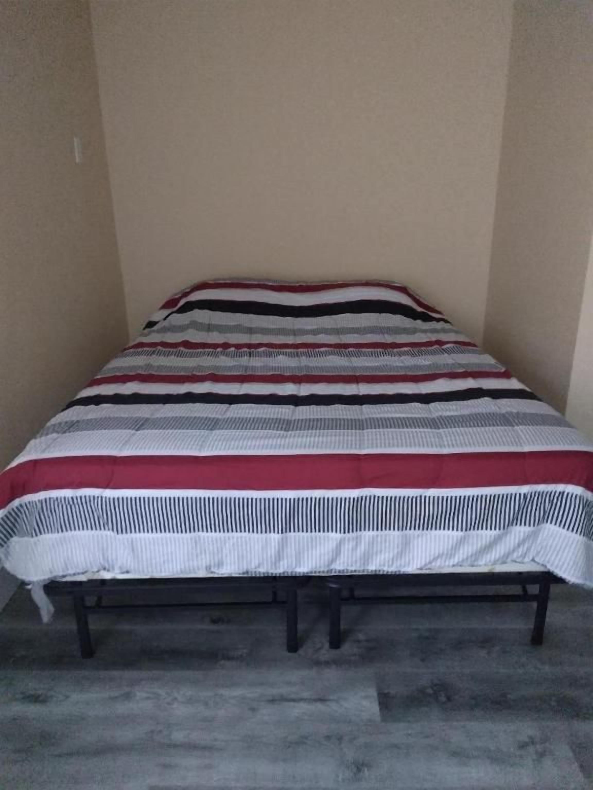 Ein Bett mit gestreifter Bettdecke in einem Raum mit schlichten Wänden und einem Betonboden.
