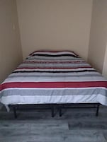 A bed with a striped bedspread in a room with plain walls and a concrete floor.