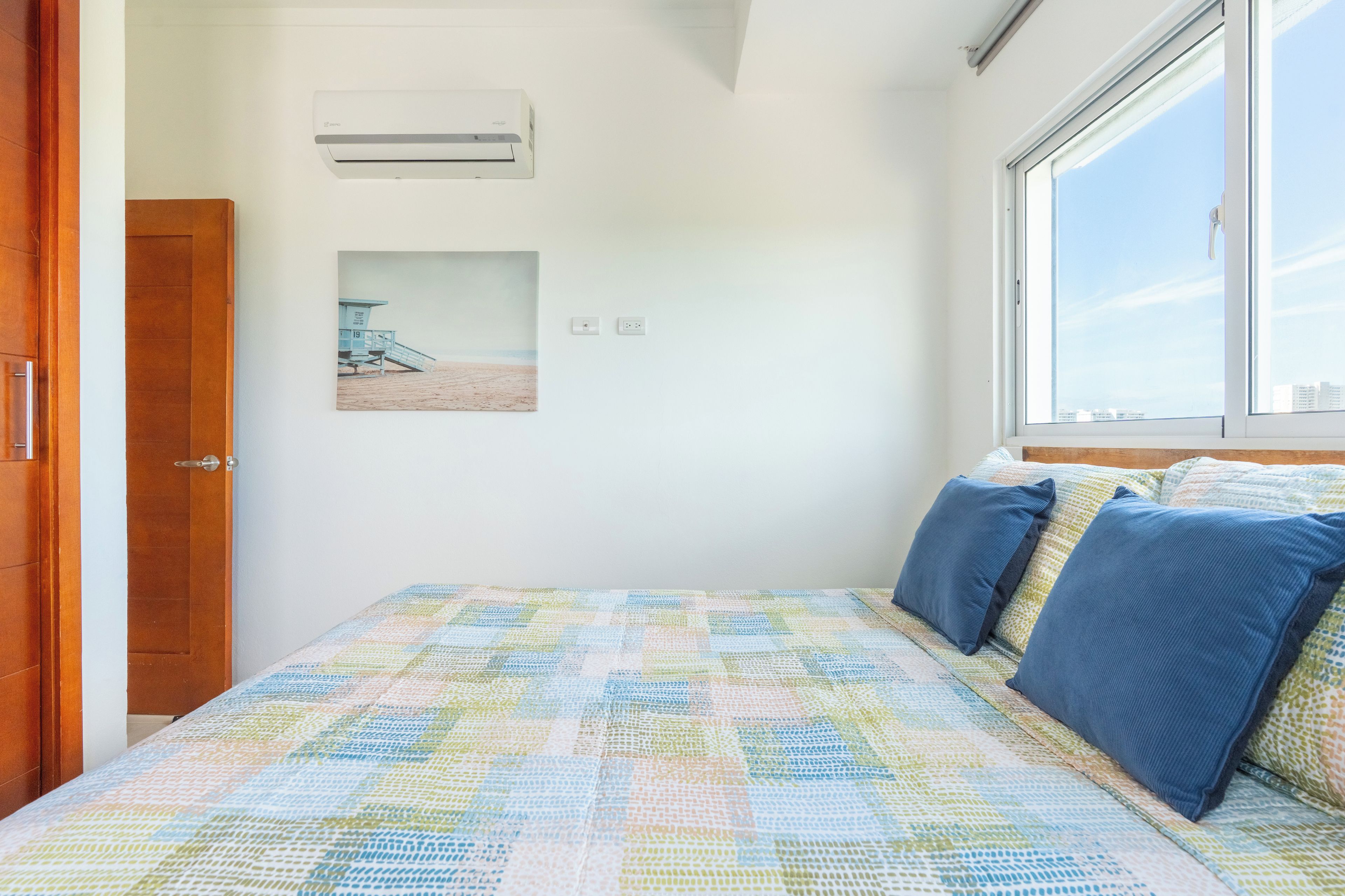 Une chambre à coucher avec un lit, une fenêtre, un climatiseur fixé au mur et un tableau encadré.