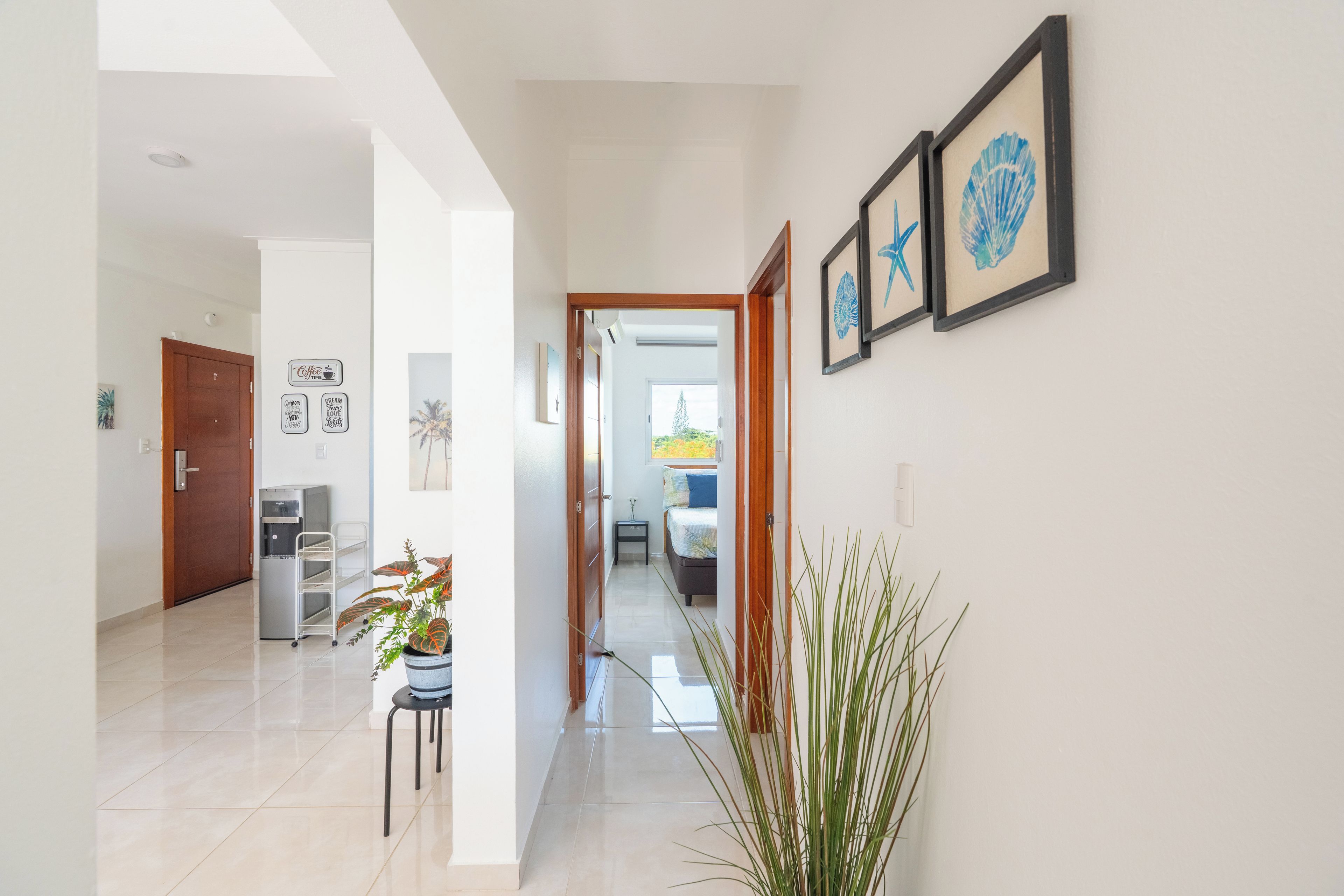 A hallway with a water dispenser, a cart, and framed artwork on the wall.