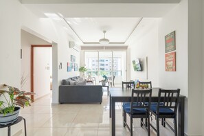 Uma sala de estar moderna com sofá, mesa de jantar, cadeiras e vista através de uma grande janela.