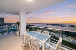 Un balcon avec une table et des chaises, offrant une vue sur le paysage urbain au coucher du soleil.