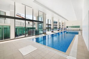 En inomhuspool med väggar av genomskinligt glas, ett kaklat golv och en modern arkitektonisk design.