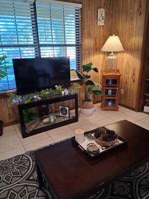 Una sala de estar con televisor, lámpara, planta y una bandeja con galletas.