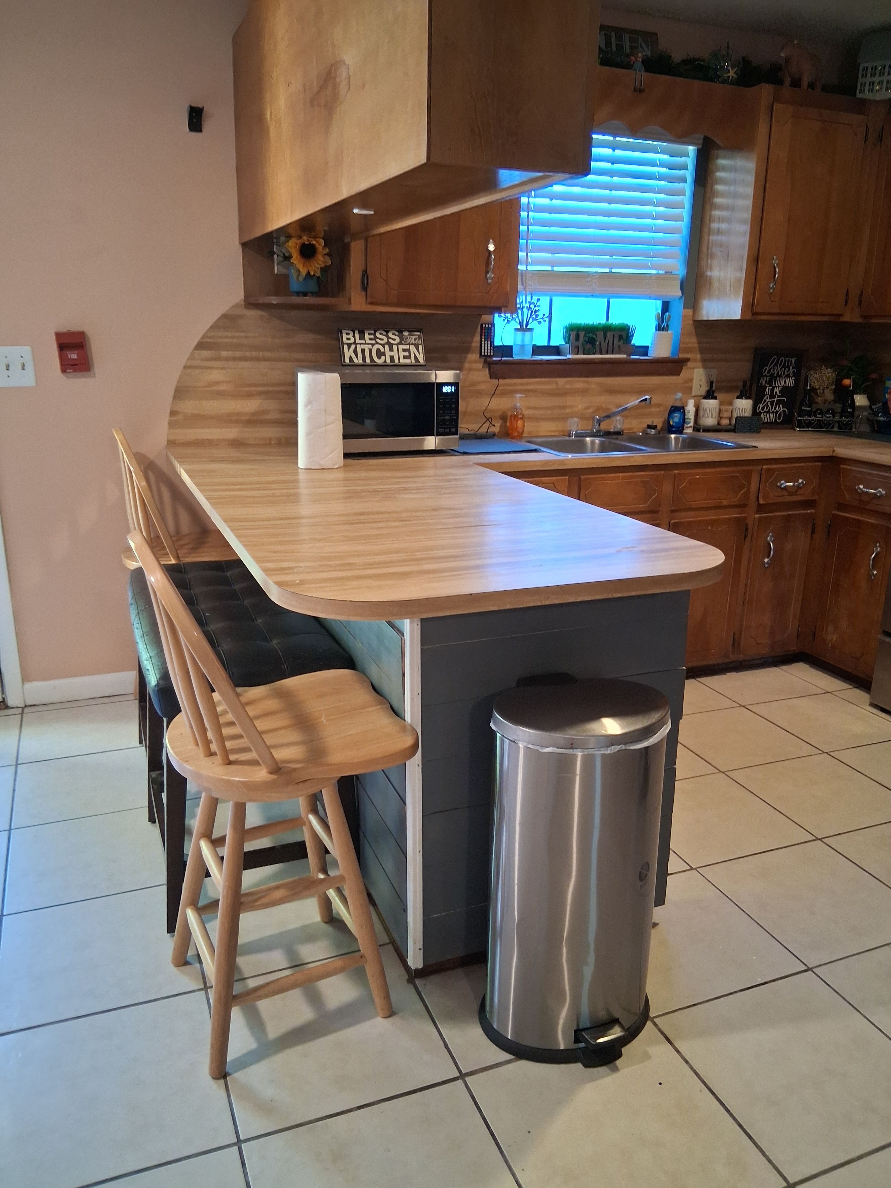 A kitchen with a wooden island, a microwave, a sink, and a trash can.