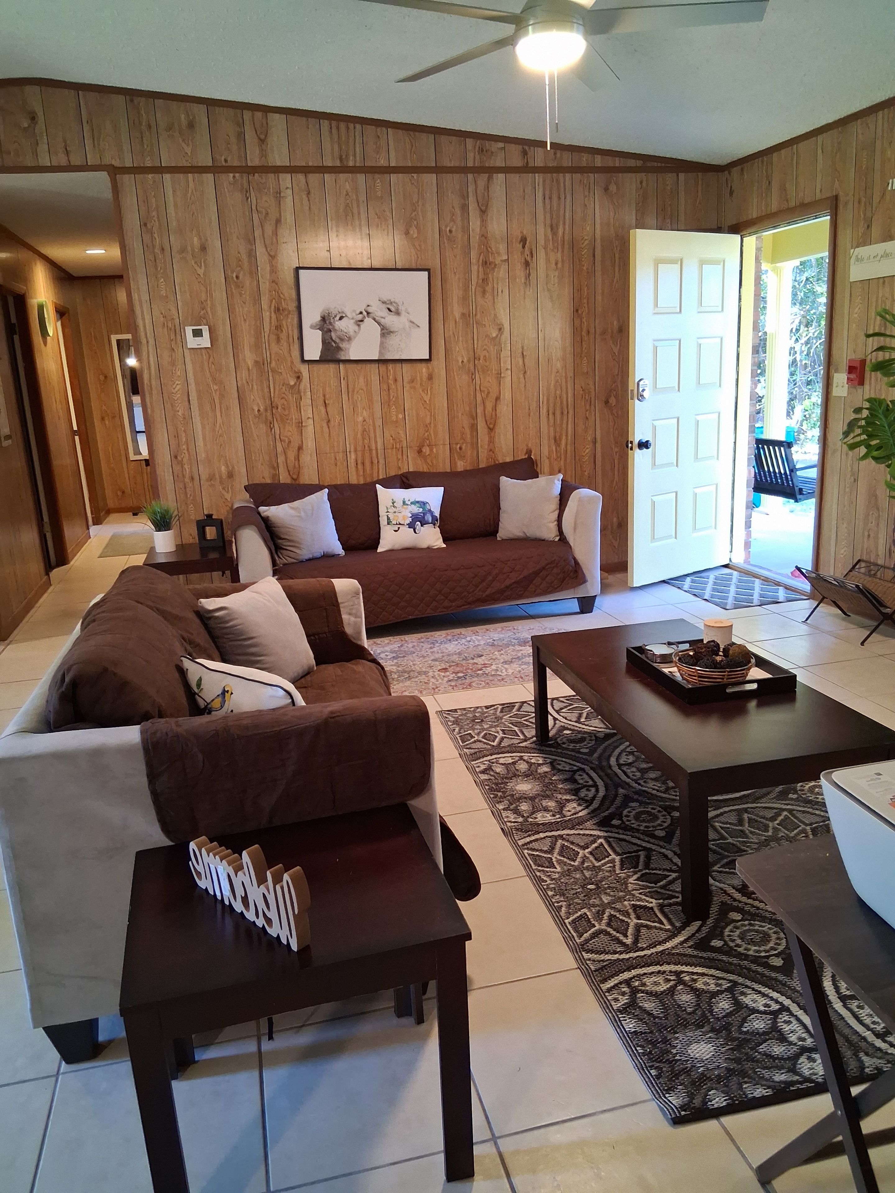 A living room with a brown sofa, a white sofa, and a coffee table. There is a door leading outside.